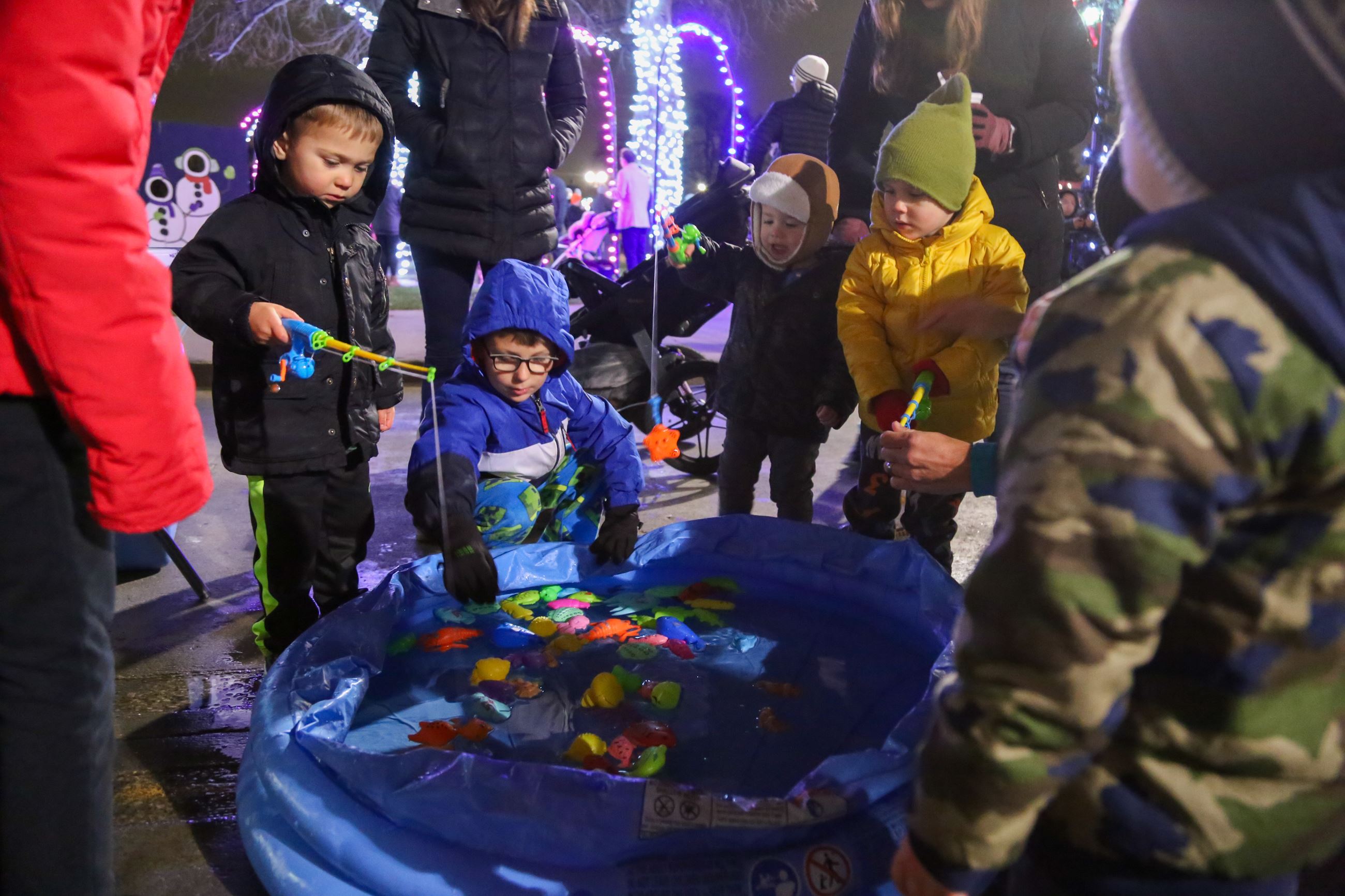 Young kids gathered around a mini pool catching plastic fish