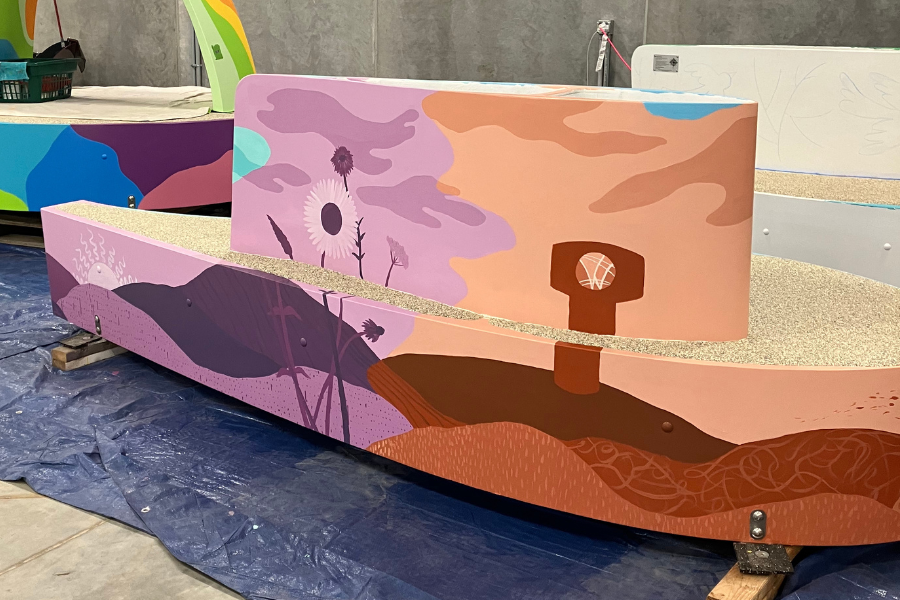 Long bench painted with scene of wildflowers in the wind and water tower with Waukee logo