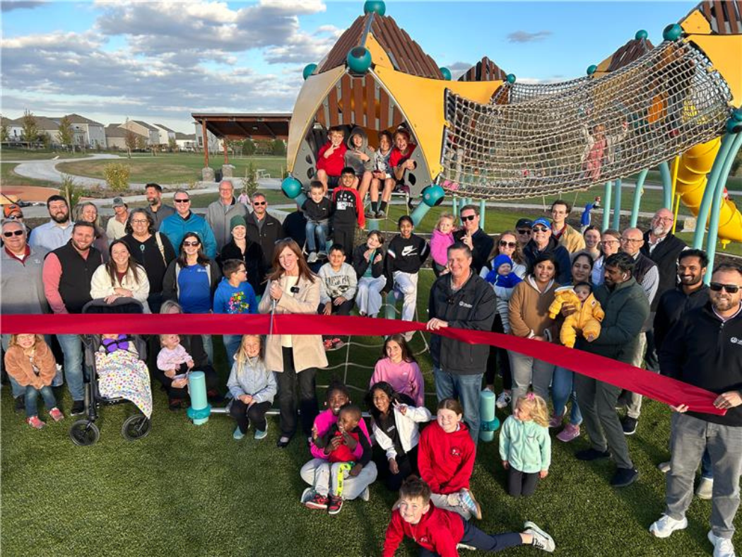 a group of people holding a ribbon in front of the treehouse structure to celebrate park opening