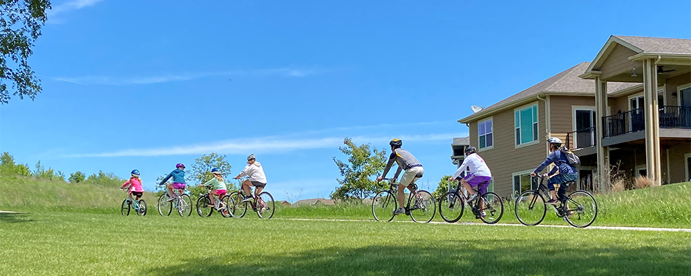 family riding bikes on trail through a nieghborhood with blue skies and green grass