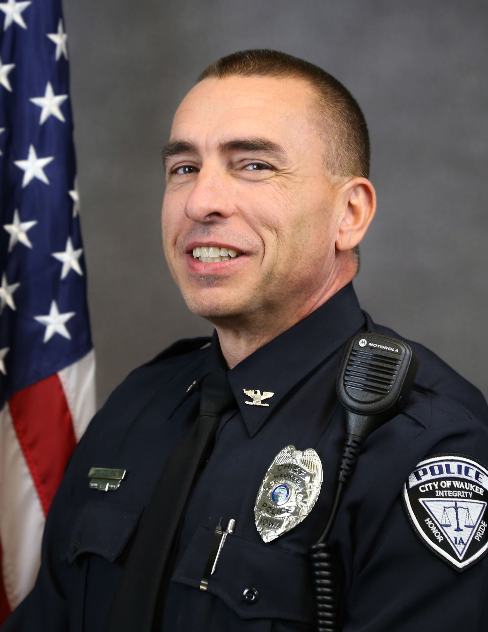 Headshot of Police Chief Chad McCluskey in front of grey background and American flag