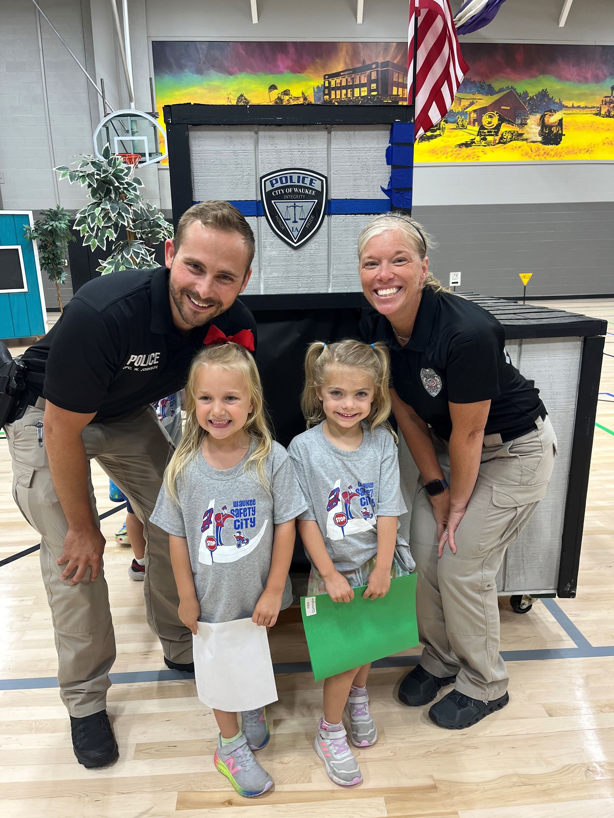 two young girls in pigtails with two police officers smiling at the camera