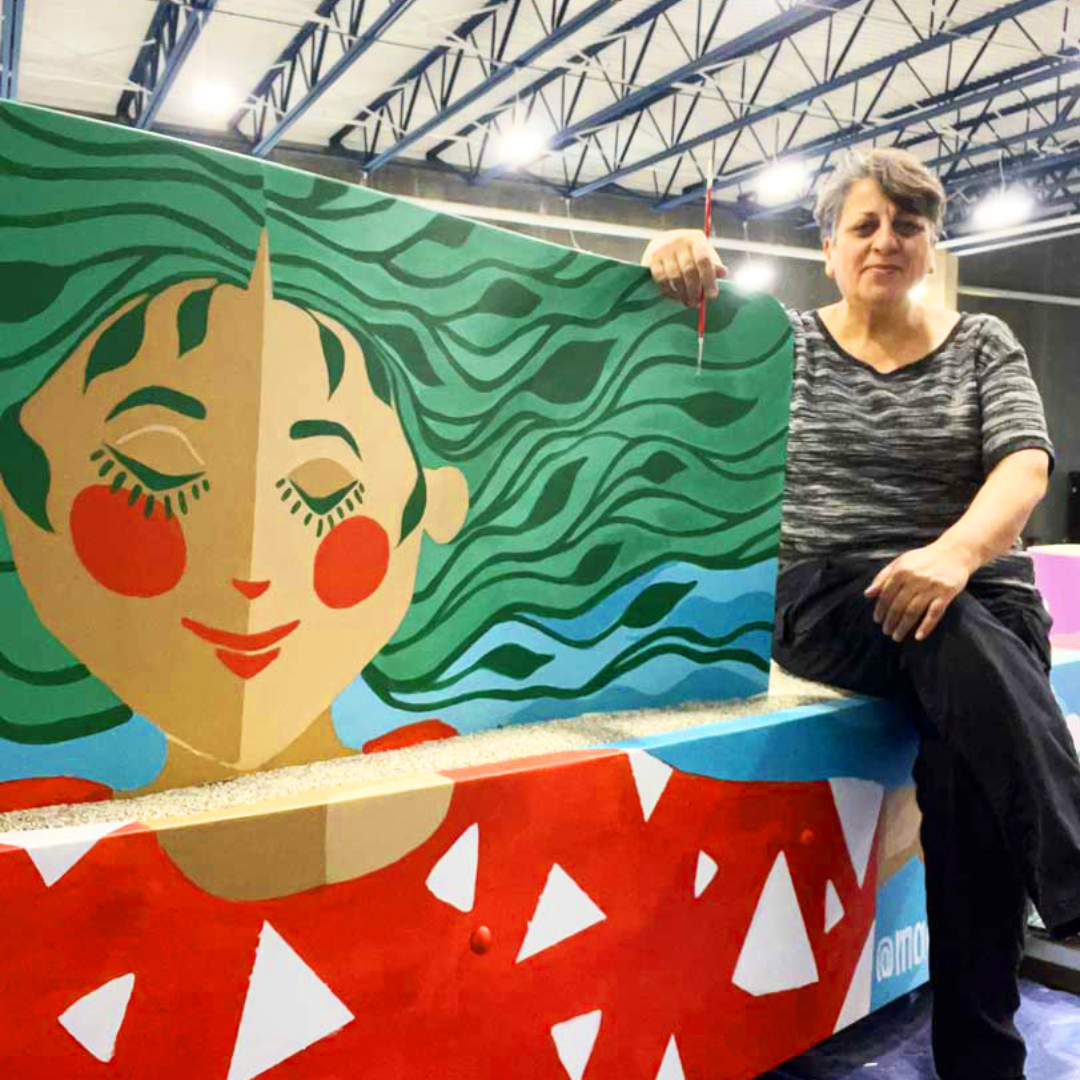 woman standing next to colorful bench she painted with woman with leaves for hair and serene smile