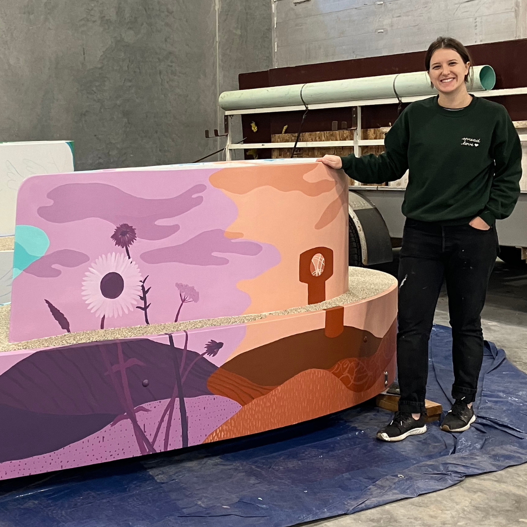 Young woman standing next to bench she painted with fall flower and water tower